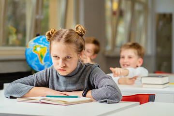 Stressed school girl child, pupil, bullying victim being by classmates in classroom during lesson...