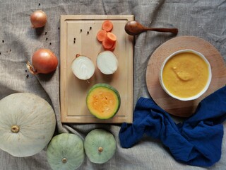 Vegetarian autumn pumpkin cream soup on burlap background with sliced vegetables