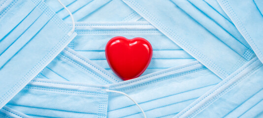 Red heart lying in pile of protective face masks. Valentine's day for lovers, couples during...
