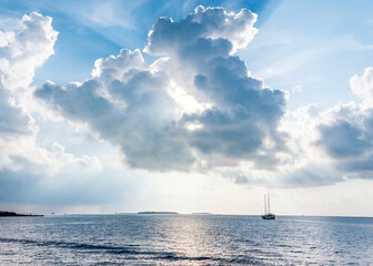 Naklejka na ściany i meble The sun shining through a picturesque clouds over the Indian ocean with Maldivian islands on the horizon and the silhouette of a ship with masts