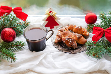 Cup of coffee with milk and cookies staying on the windowsill with christmas tree and decorations