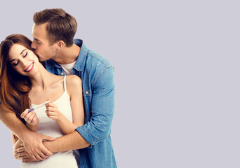 Love, relationship, lovers, family concept - happy couple, finding out results of a pregnancy test. Man kissing woman. Grey background. Copy space for text.