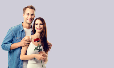 Love, relationship, dating, flirting, romantic concept - portrait of young happy smiling embracing couple with flower. Isolated over grey background.