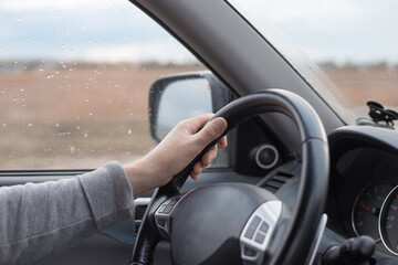 Male hand on the steering wheel of a Mitsubishi car. Autumn rain outside the window. Comfortable...