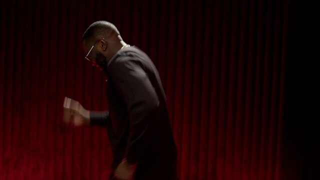Slo-mo African for music video. African American man dancing in the studio in a bright image. The expressive dancer moves effectively on the studio video. Portrait of a handsome guy dancing on a red b