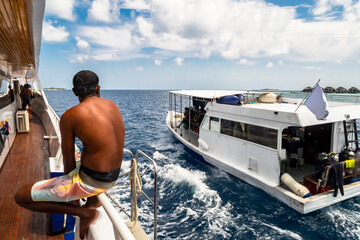 A tanned sailor sitting on the railing of the ship looks at a passing ship with diving equipment