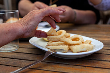 Mano que coge un delicioso calamar frito y servido sobre plato en la mesa de un restaurante