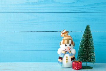 Cute snowman and gift with christmas tree on blue wooden background.