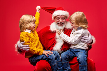 kids and santa claus man have fun together, isolated on red studio background. magic, wishes, xmas gifts, happy new year concept