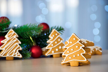 Traditional gingerbread in Christmas tree shape with white icing and fir branches, red toys and bokeh lights on background. Handmade Christmas cookies, taste of childhood. Festive mood and spirit.