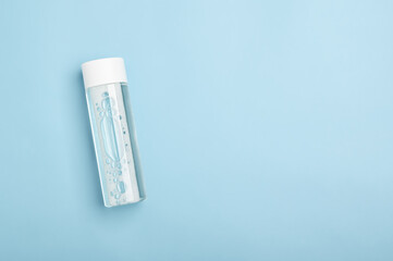 Micellar water, lotion in a white plastic packaging bottle on a blue background. Cleansing cosmetic beauty product with foam top view. Refreshing facial skincare. Transparent skin moisturizer