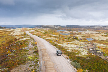 Aerial panoramic view of winding road among tundra landscape in autumn. Beautiful nature scenery of Russian North. Small cargo truck driving on gravel way. Kola Peninsula, Murmansk Oblast, Russia