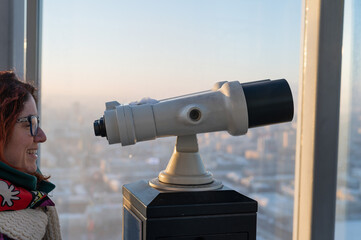 A woman looks through binoculars on the observation deck of a skyscraper