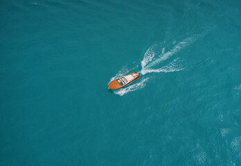 Wooden runabout in the rays of the sun on turquoise water. Drone view of a boat  the blue clear waters. Top view of a wooden boat sailing to the blue sea. Classic Italian motorboat.