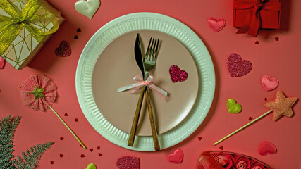 Valentine's day table setting, white plate surrounded by cutlery and decorative hearts on a red background. Top view, flat lay, copy space. Valentine's day congratulations 