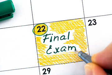 Woman fingers with pen writing reminder Final Exam in calendar.