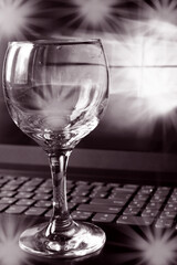 black and white photo of one empty wine glass on a laptop keyboard with highlights