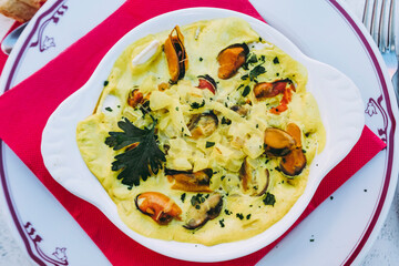 Gratins de moules fraîches sauce oignons persil et riz dans un plat à gratin blanc