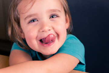 Close-up portrait of cheerful caucasian toddler girl showing tongue, funny kids face