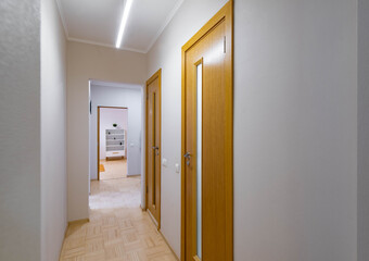 Modern interior of narrow hallway in luxury apartment. Wooden doors to the rooms. White walls.