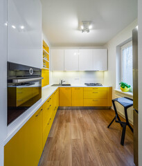 Fototapeta premium Modern interior of kitchen in luxury apartment. Yellow kitchen set with white counter. Black sink. Gas stove. Oven. Cabinets and drawers.