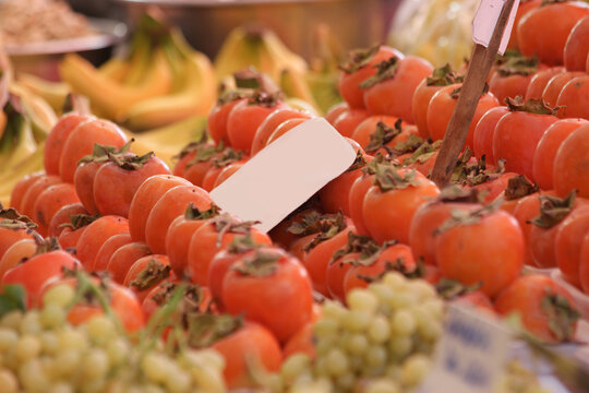Street market with fresh colorful fruits on display. Persimmons and grapes for sale at market counter.