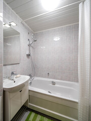 Modern light interior of bathroom in apartment. White tile. Bath tub, sink and mirror. Green mat.