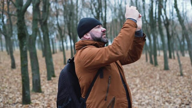 man with a beard in the forest makes nature photos on the phone.