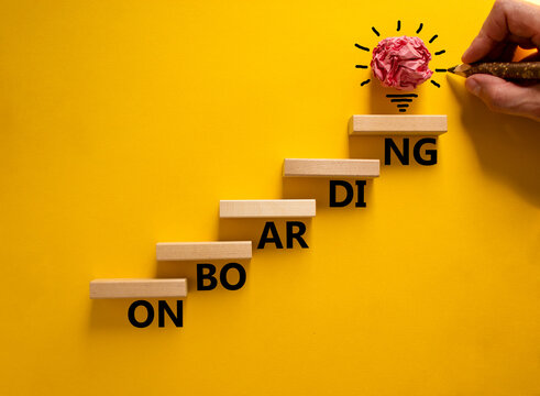 Success onboarding process symbol. Wood blocks stacking as step stair on yellow background, copy space. Businessman hand and light bulb. Word 'onboarding'. Business and onboarding concept.