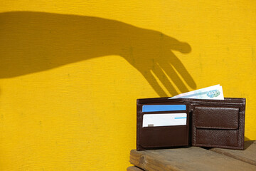 Shadow of hand on yellow wall trying to steal a leather wallet with banknote and credit cards....