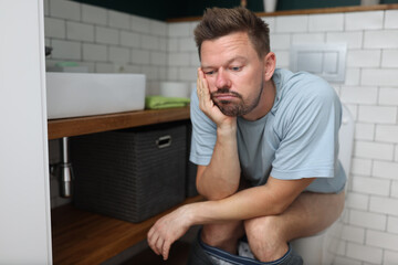 Man sit on toilet with constipation and wait for laxative to take effect. Digestive system disease and treatment. - obrazy, fototapety, plakaty