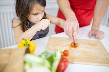 Little girl and her father slicing vegetables on a cutting board