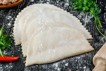 Raw chebureks with meat, cooked for frying on a wooden table