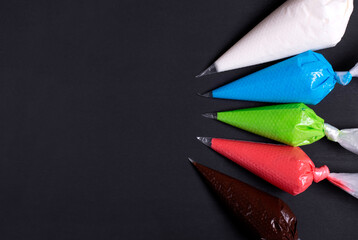 Multicolored glazing in icing bags on the black table. White, blue, green, red and chocolate sugar icing. Copy space. Set for decorating desserts