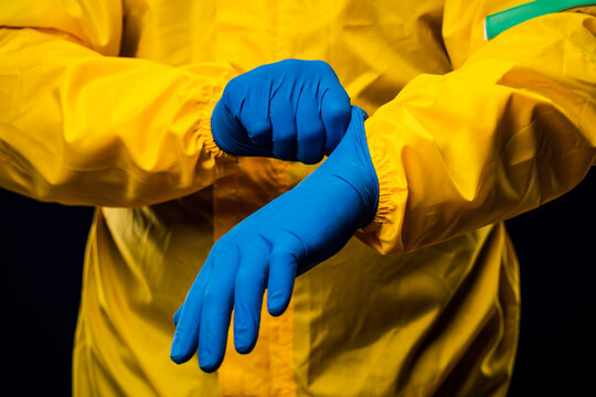 The scientist wears a yellow decontamination suit and wears blue rubber gloves to protect his skin.