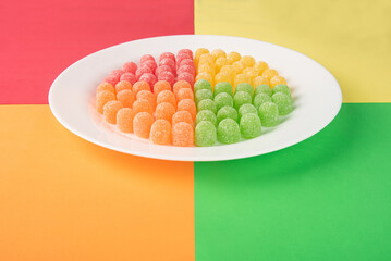 Gummy candy, arrangement of gummy candy arranged by color on a white plate on a colored surface.