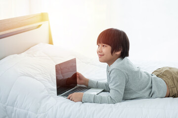 Asian boy in front of laptop computer lay on bed with smile.