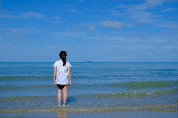 Back side of a girl standing in the sea looking at the horizon.