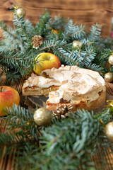 gedeckter Kuchen mit Apfel und Marzipan mit einer Haube aus Baiser auf einem Tisch aus Holz zur Weihnachtszeit mit Zweigen von der Tanne oder einem Nadelbaum