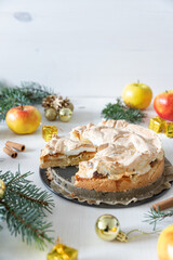 gedeckter Kuchen mit Apfel und Marzipan mit einer Haube aus Baiser auf einem Tisch aus Holz zur Weihnachtszeit mit Zweigen von der Tanne oder einem Nadelbaum