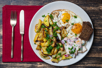 Ukrainian food, fried potatoes with onions, eggs, vegetable salad, black bread on wooden background