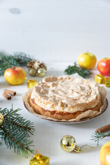 gedeckter Kuchen mit Apfel und Marzipan mit einer Haube aus Baiser auf einem Tisch aus Holz zur Weihnachtszeit mit Zweigen von der Tanne oder einem Nadelbaum