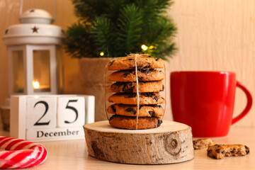 Beautiful Christmas postcard with chocolate cookies on wooden stand, red cup, Christmas tree, latern and calendar dated December 25. Festive, holiday mood. Close-up