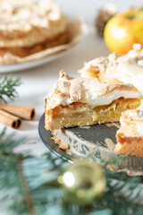 gedeckter Kuchen mit Apfel und Marzipan mit einer Haube aus Baiser auf einem Tisch aus Holz zur Weihnachtszeit mit Zweigen von der Tanne oder einem Nadelbaum