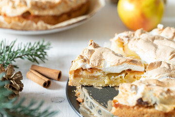 gedeckter Kuchen mit Apfel und Marzipan mit einer Haube aus Baiser auf einem Tisch aus Holz zur Weihnachtszeit mit Zweigen von der Tanne oder einem Nadelbaum
