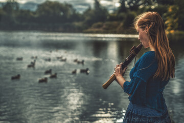 beautiful shamanic girl playing on shaman flute in the nature. © jozefklopacka