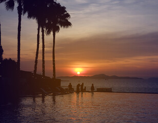 Silhouette swimming pool at sunset with happy tourist on holidays.