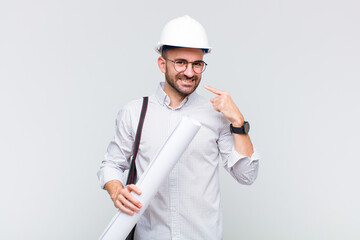 young bald man smiling confidently pointing to own broad smile, positive, relaxed, satisfied attitude