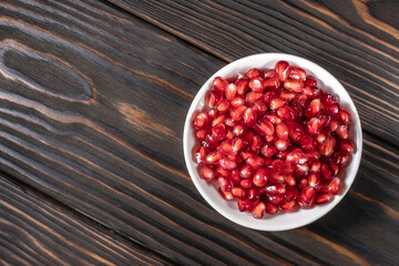 Garnet seeds in white plate on dark wooden background
