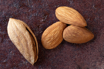 One whole unpeeled almond, and three peeled nuts dark red background.